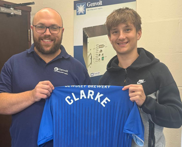 Alex Clarke of Bewdley Town FC celebrates new sponsorship deal with Genvolt with Genvolt Operations Manager Kieran Woodhouse by holding up a football shirt in the office